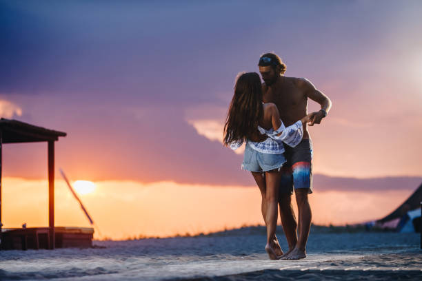 Young loving couple having fun while dancing during a beach holiday at sunset.