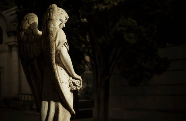 old statue of angel in cemetery with sunlight and shadow - morbid angel stok fotoğraflar ve resimler