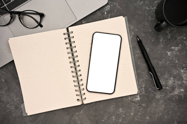 istock Workspace top view with smartphone mockup, spiral notebook on grey cement background. 1400020171