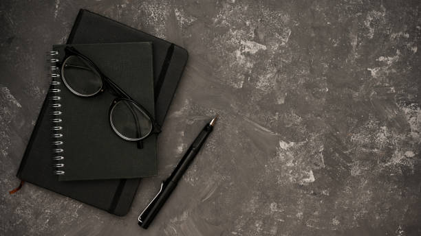 istock Stylish black spiral notebook, glasses, pen and copy space on grey cement background. 1400020211