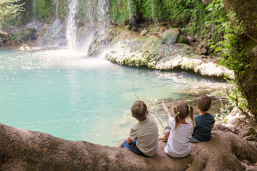 Children in nature park at a waterfall enjoying nature, happiness together