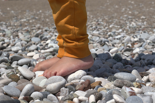 Little barefoot kid walking on the stone at the pebble beach. Children's hardening and rehabilitation