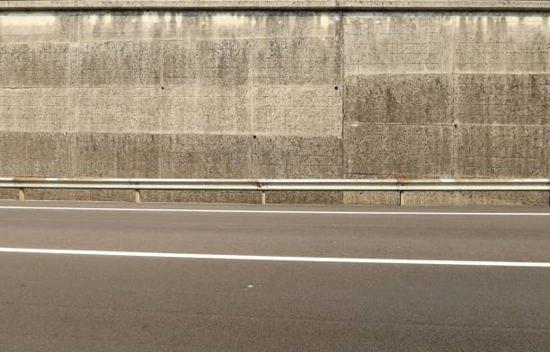 metallische leitplanke vor einer groben hohen betonwand. zweispurige asphaltstraße vorne - empty nobody two lane highway highway stock-fotos und bilder