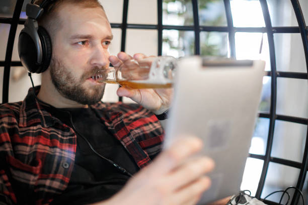 jeune homme avec casque utilisant une tablette numérique et buvant de la bière sans alcool à la maison - non alcoholic beverage audio photos et images de collection