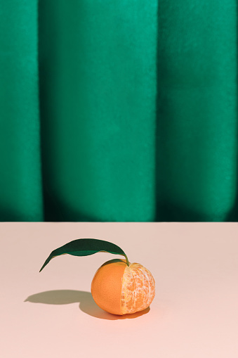 Half peeled tangerine fruit against green satin curtain. Artistic still life, freshness concept.