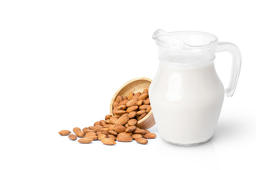 Glass jug of Almond milk with almond nuts in wooden bowl isolated on white background.