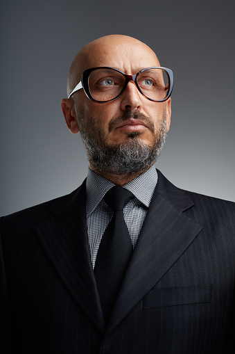 Studio portrait of a middle-aged bearded businessman with funny eyeglasses posing against a dark background
