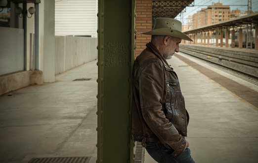 Portrait of adult man in cowboy hat waiting in train station.