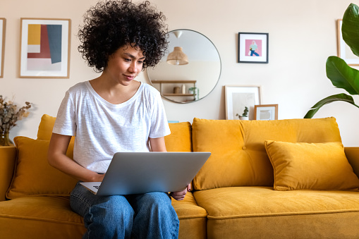 Young African american woman sitting on the couch using laptop working at home. Copy space. Technology and lifestyle concepts.