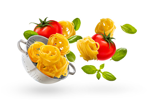 Front view of various Italian ingredients such as basil, tomatoes and pasta levitating with a pasta colander on white background