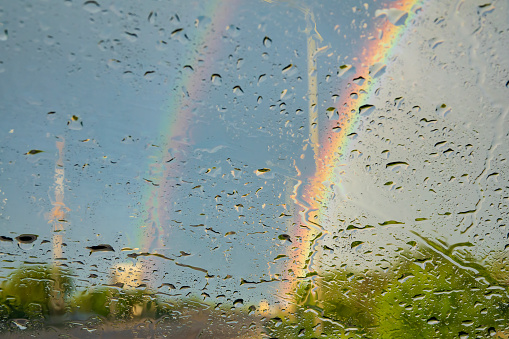 Raindrops and rainbow on the car wind glass. Driving in rainy day concept. Creative background