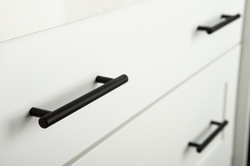 Custom white wooden cabinet drawer with black handles underneath quart kitchen island.