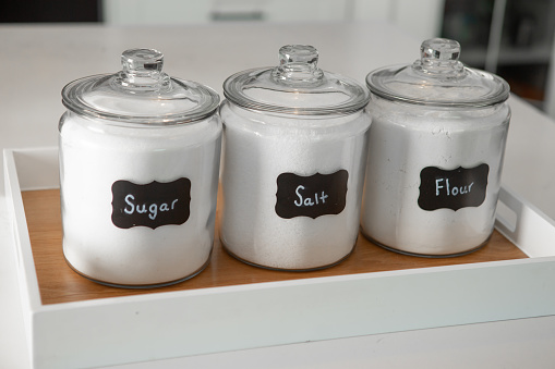 Condiment jar storage with retro name label in wooden tray on domestic kitchen white counter