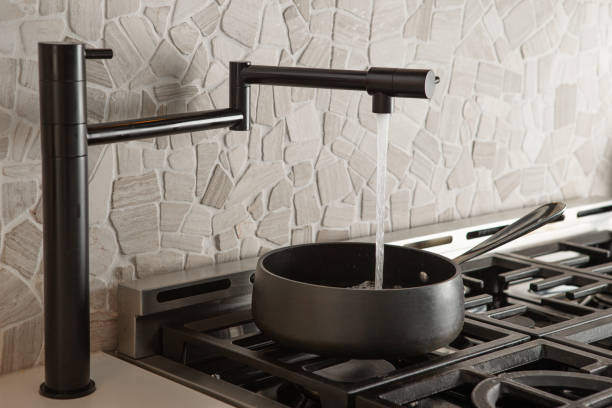 Black pot filler faucet over stove Black pot filler faucet filling up water in cooking pot on gas stove in kitchen with stone back splash image of modern kitchen with black granite worktop gas hob cooker stock pictures, royalty-free photos & images