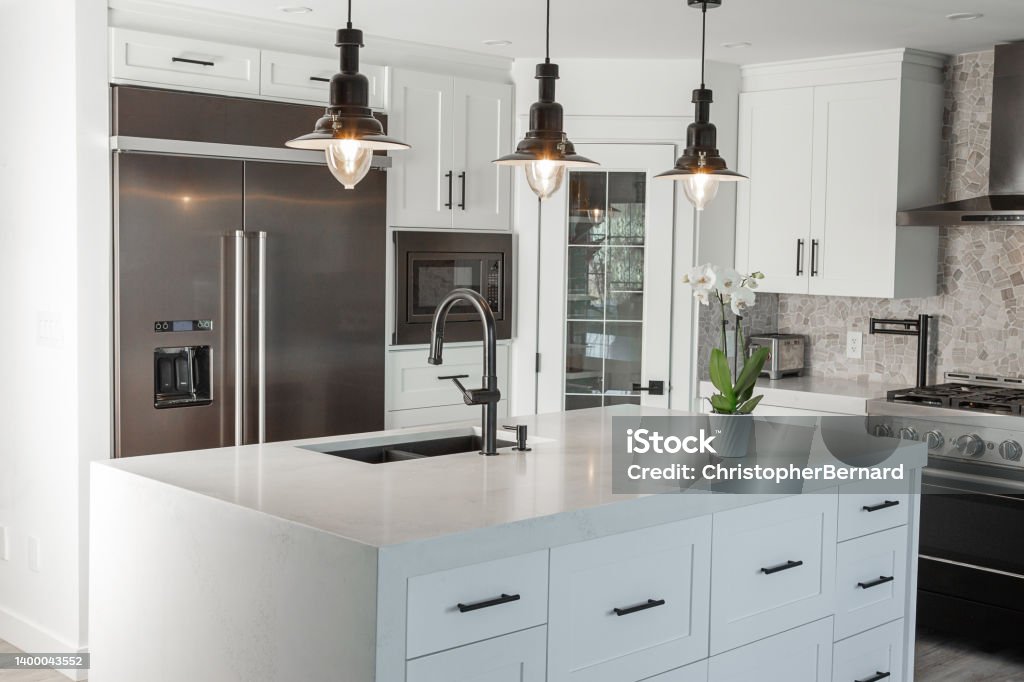 Black and white modern kitchen Black pendent lights over quartz counter top with over size stainless fridge in this newly renovated kitchen. Kitchen Stock Photo