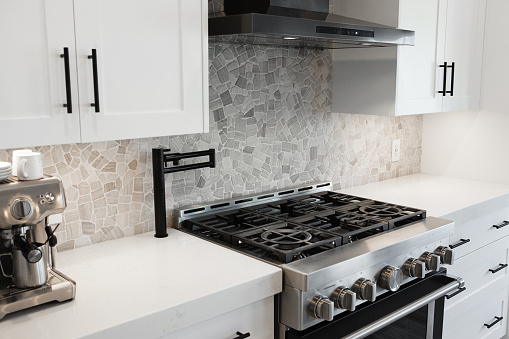 Black pot filler faucet over 6 burners gas stove in modern kitchen with stone back splash and with black hood fan