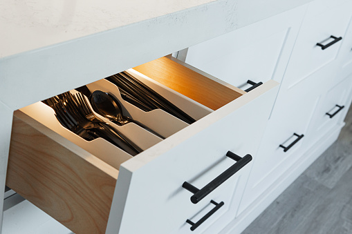 Black utensil organized in custom white wooden cabinet drawer with black handles under quart kitchen island.