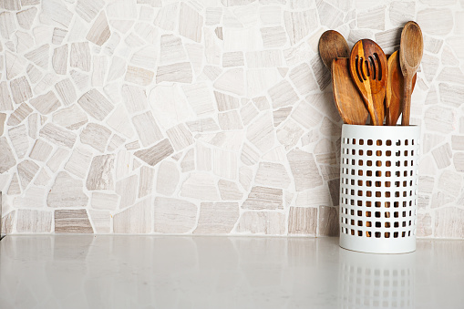 Cooking utensil on quartz domestic kitchen counter with stone backsplash.