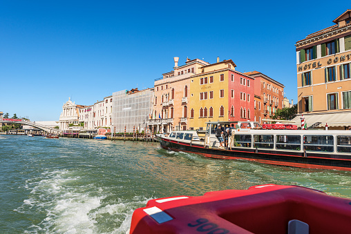 Venice, Italy - June 2, 2021: Two ferry boats and a water taxi in motion in the Grand Canal (Canal Grande) near the railway station. UNESCO world heritage site, Venetian lagoon, Venice, Veneto, Italy, Europe. A large number of tourists aboard the small ferry on a sunny spring day, on background the church of Santa Maria di Nazareth or degli Scalzi and the bridge called Ponte degli Scalzi.