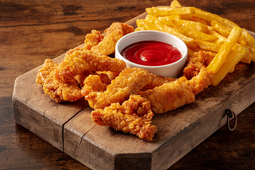 Chicken tenders, breaded nuggets, with a bbq dip and French fries, on a wooden background
