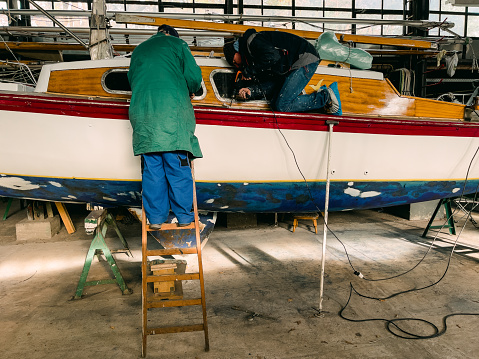 One senior and one mature man work together, maintaining sailing yacht, boathouse, DIY, Germany