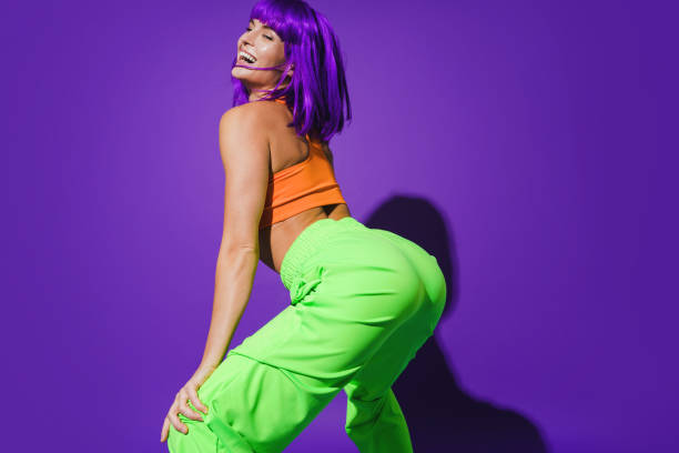 mujer despreocupada con colorido twerking de ropa deportiva sobre fondo púrpura - como bailar perreo fotografías e imágenes de stock
