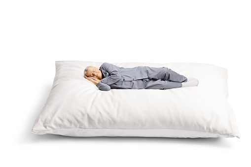 Elderly man in pajamas sleeping on a big pillow isolated on white background