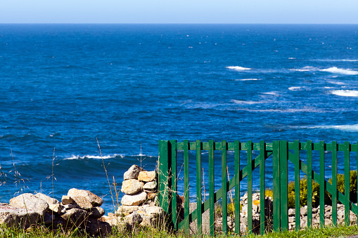 Tranquil seascape, waves, rocky coastline  and green wooden fence near Muxía village, Finisterre headland area, Costa da Morte, A Coruña province, Galicia, Spain.  Horizon over Atlantic ocean.