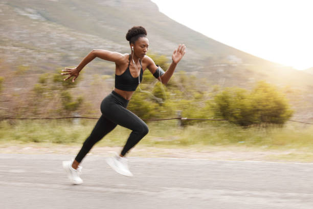 flou de mouvement corps entier s’adapte active femme afro-américaine courant rapidement tout en faisant de l’exercice à l’extérieur dans la nature. femme noire athlétique forte sprintant pendant l’entraînement tout en écoutant de la musique a - fast motion photos photos et images de collection