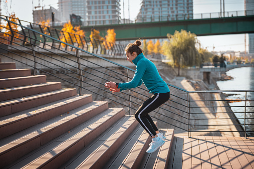 Young woman in sports clothes jumping up the stairs on city waterfront, exercise for healthy urban lifestyle