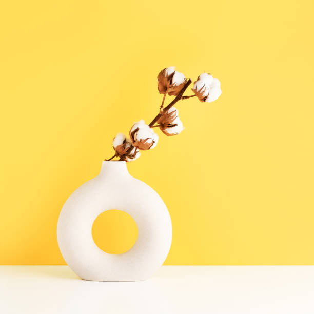istock Round vase with a cotton branch on a white table by the yellow wall. Copy space for text 1400050601