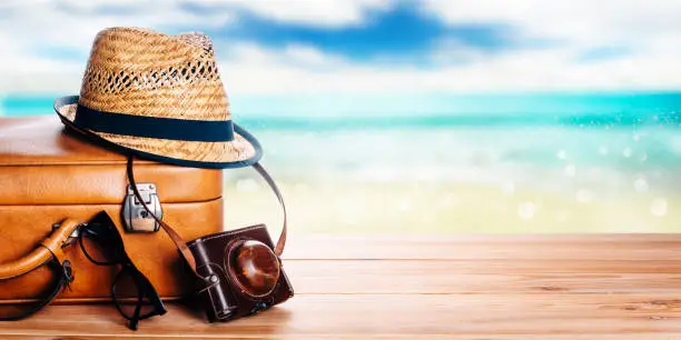 Photo of Vintage suitcase, sunglasses and hipster hat wooden deck and blur tropic sea background