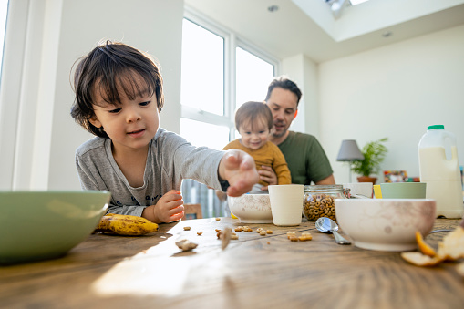 A front-view shot of a father and his two young boys spending time together around a dining table in the north east of England. They are enjoying breakfast.