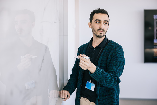 Portrait of Young entrepreneur writing new ideas on office whiteboard. Tech start-up enterprise.