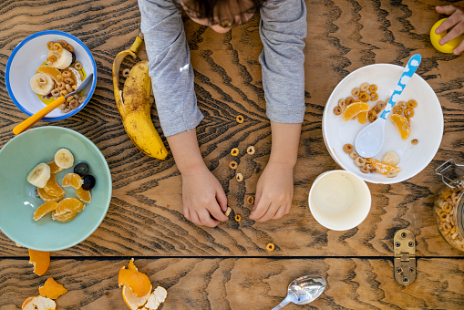 A directly above shot of an unrecognisable young boy at a dining table in the north east of England. He is reaching his arms out to play with his morning breakfast cereal.