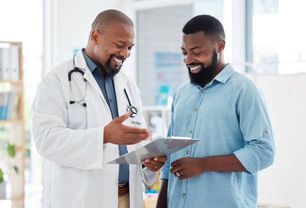 Young patient in a consult with his doctor. African american doctor showing a patient their results on a clipboard. Medical professional talking to his patient in a checkup stock photo