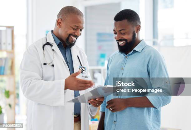 Young Patient In A Consult With His Doctor African American Doctor Showing A Patient Their Results On A Clipboard Medical Professional Talking To His Patient In A Checkup Stock Photo - Download Image Now