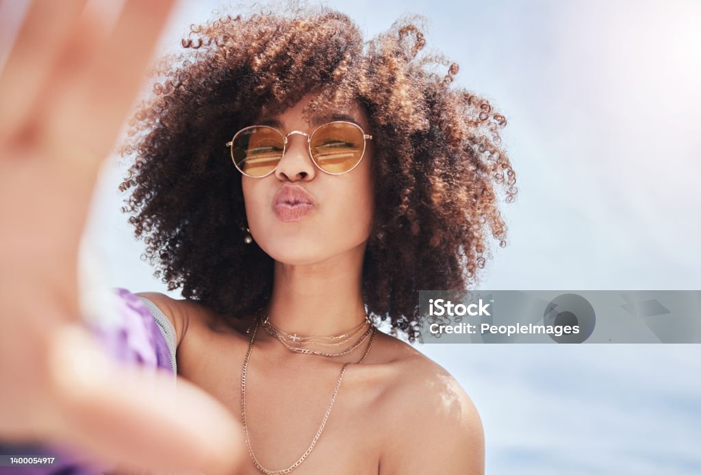 Porträt einer jungen, trendigen, schönen gemischtrassigen Frau mit einem Afro, der lächelt und draußen für ein Selfie posiert. Hispanische Frau mit Sonnenbrille, die glücklich aussieht. Modische afroamerikanische Frau in der Stadt - Lizenzfrei Frauen Stock-Foto