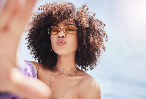 Retrato de una joven mujer de raza mixta hermosa y de moda con un afro sonriendo y posando para una selfie afuera. Mujer hispana con gafas de sol luciendo feliz. Mujer afroamericana de moda en la ciudad photo