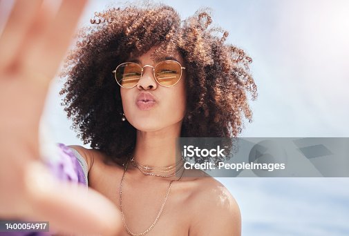 istock Portrait of young trendy beautiful mixed race woman with an afro smiling and posing for a selfie outside. Hispanic woman wearing sunglasses looking happy.Fashionable African American woman in the city 1400054917