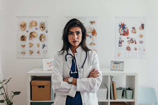 Portrait of the serious female doctor standing in her office at clinic and looking at camera