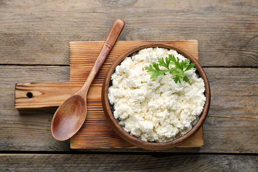 Delicious fresh cottage cheese with parsley on wooden table, top view