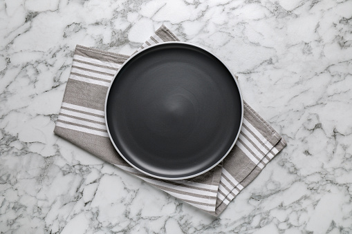 New dark plate and napkin on white marble table, top view