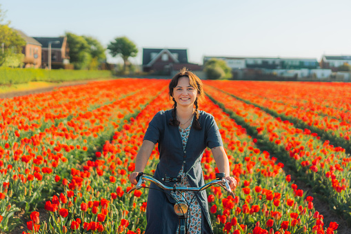 Young Caucasian woman riding on bicycle on tulip field in the Netherlands