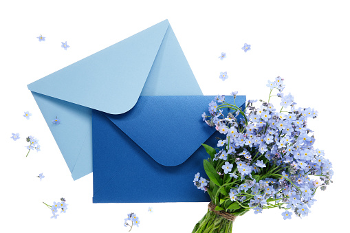 Blue envelope with wedding invitation card or birthday letter decorated with bouquet of wild forget me not flowers on white. Flat lay. Top view.