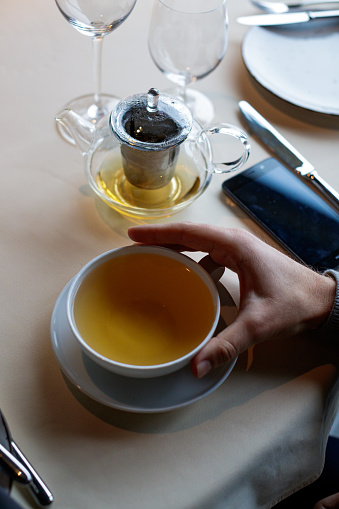 Hand holding a cup of hot tea on saucer at place setting on the restaurant table