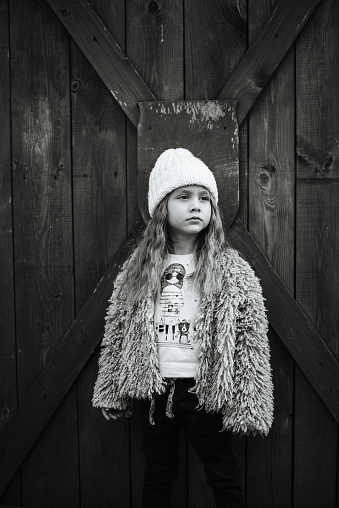 Stylish, four-year-old girl with long hair posing on a wooden background. Portrait of a beautiful baby. Fashionable children. Black and white photo