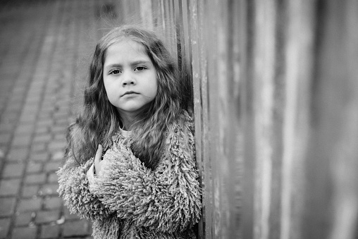 Black-and-white portrait of a cute little girl. Little girl in an urban setting with sad eyes looks at the camera