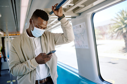 Black businessman travelling alone. A young african american businessman using a cellphone while standing in the passage on a train during his commute to the city