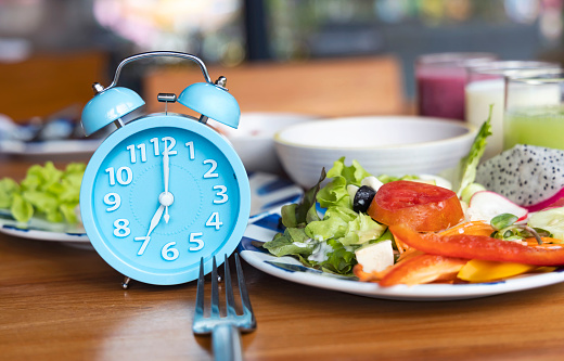 Selective focus of  Blue alarm clock Intermittent fasting eight hour feeding window concept and eating a healthy food background